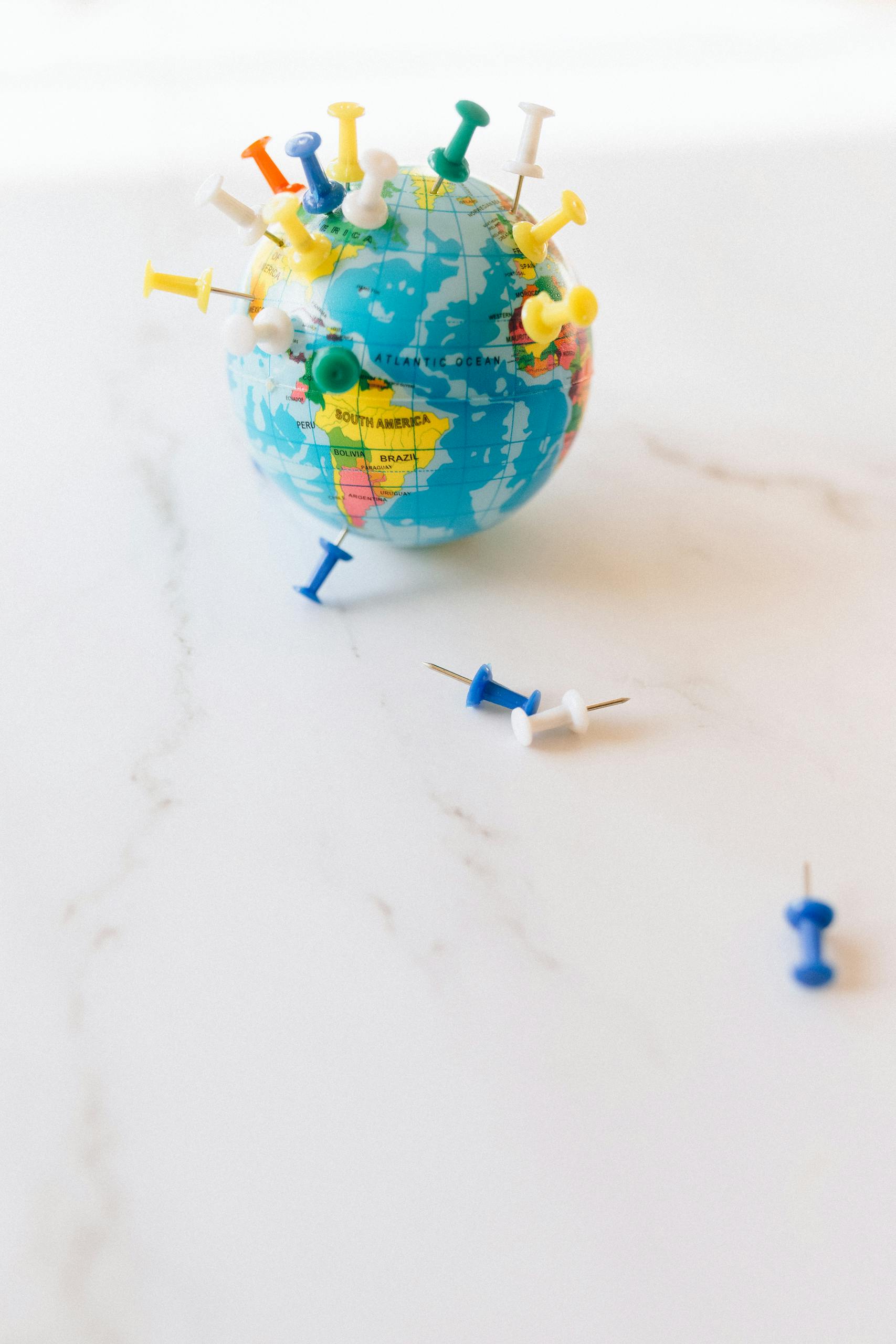 A small globe adorned with colorful pins, symbolizing travel and world exploration.